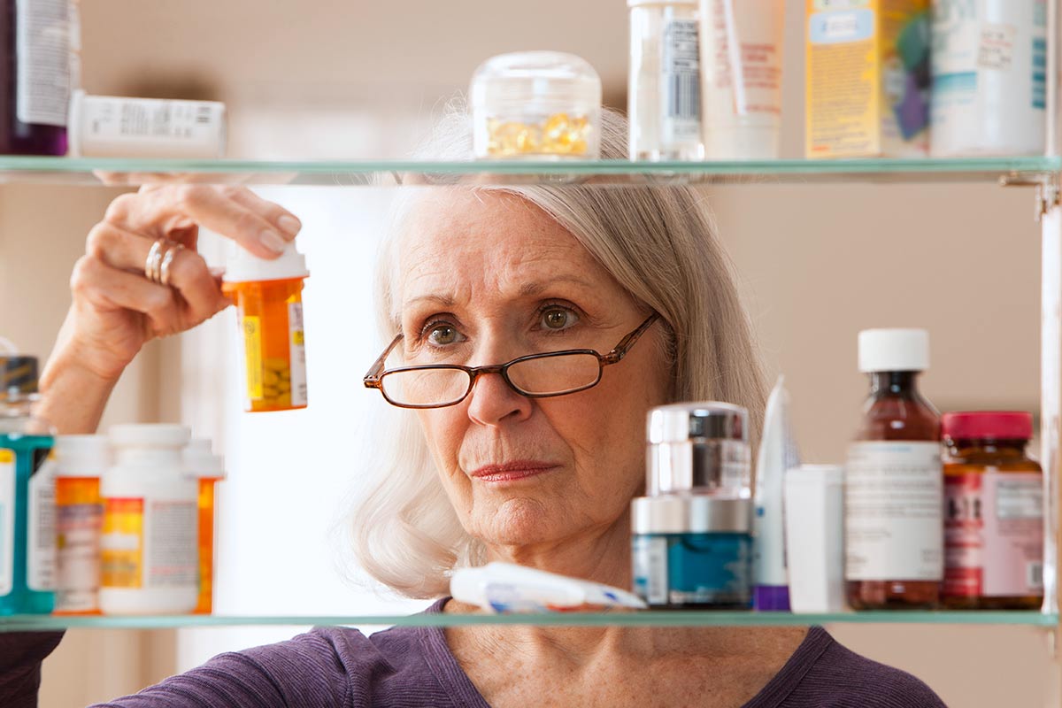 elderly woman looking at prescription medication in medicine cabinet