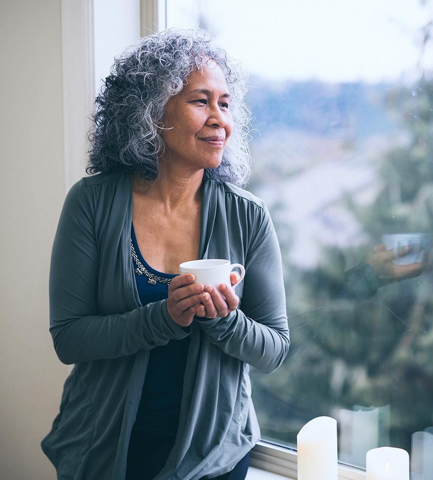 elderly woman looking out the window holding a coffee mug